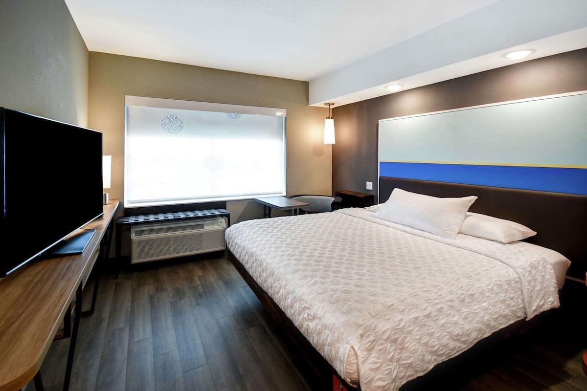Une chambre d’hôtel équipée d’un lit, d’une télévision, d’un radiateur, d’une fenêtre et d’une lampe fixée au mur.