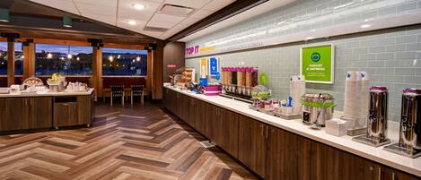 A breakfast area with a counter displaying yogurt and oatmeal, a view of the cityscape through large windows, and a herringbone wood floor.