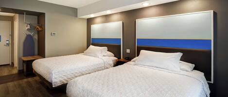 Habitación de hotel con dos camas, un banco de madera, perchero y espejo con una franja azul.