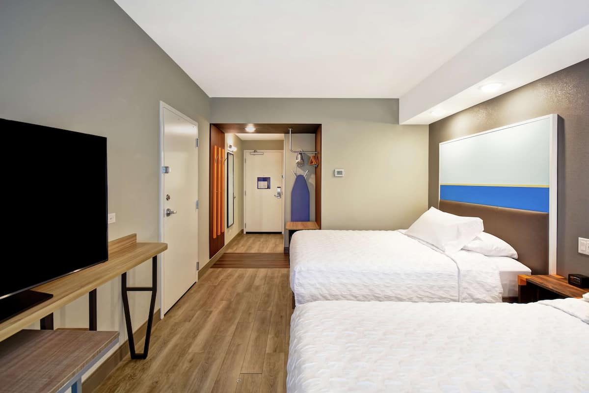 Une chambre d’hôtel avec deux lits, une télévision, un bureau et une porte donnant sur une salle de bain.