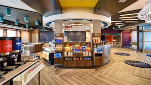 Eine Hotelhalle mit einer zentralen Kiosk-Einheit, die Snacks verkauft, einer Kaffeestation und einer Sitzecke mit Tischen und Stühlen.