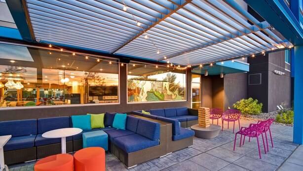Ein Außenbereich mit Sitzgelegenheiten in Blau und Orange, einer überdachten Terrasse und Lichterketten.
