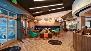Eine moderne Hotellobby mit einer Rezeption, einer Sitzecke mit bunten Stühlen und einem großen Wandgemälde.