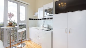 A modern kitchen with white cabinets, a microwave, and a dishwasher. There is a balcony with a potted orchid and a small table. - Vesper Apartments (Cape Town)
