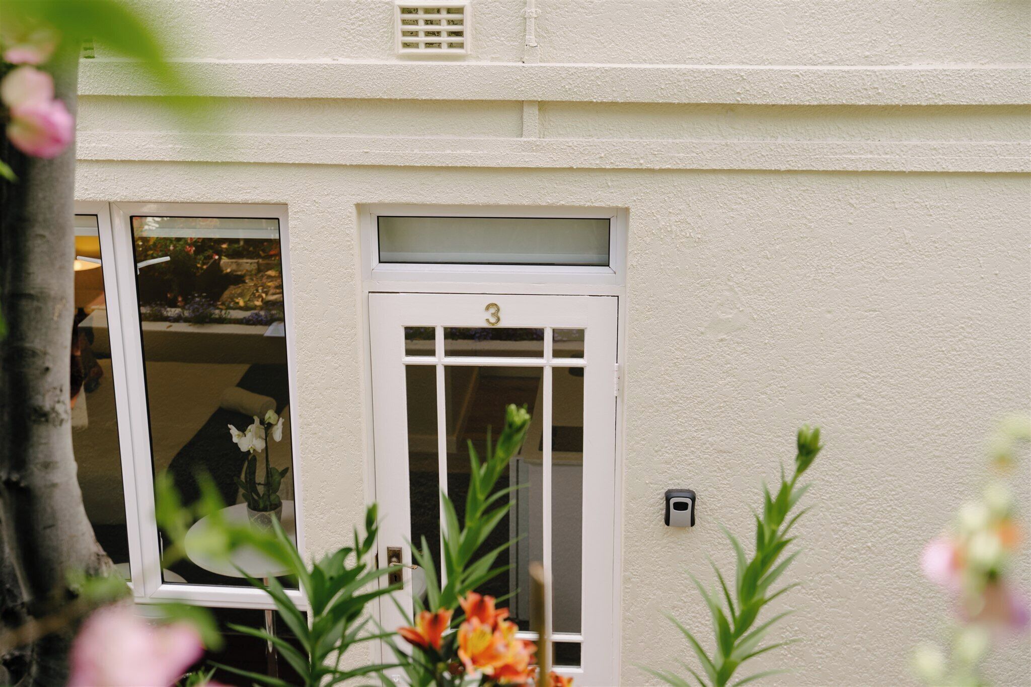 A building with a white exterior, a window with a number '3' above it, and a small outdoor area with plants.
