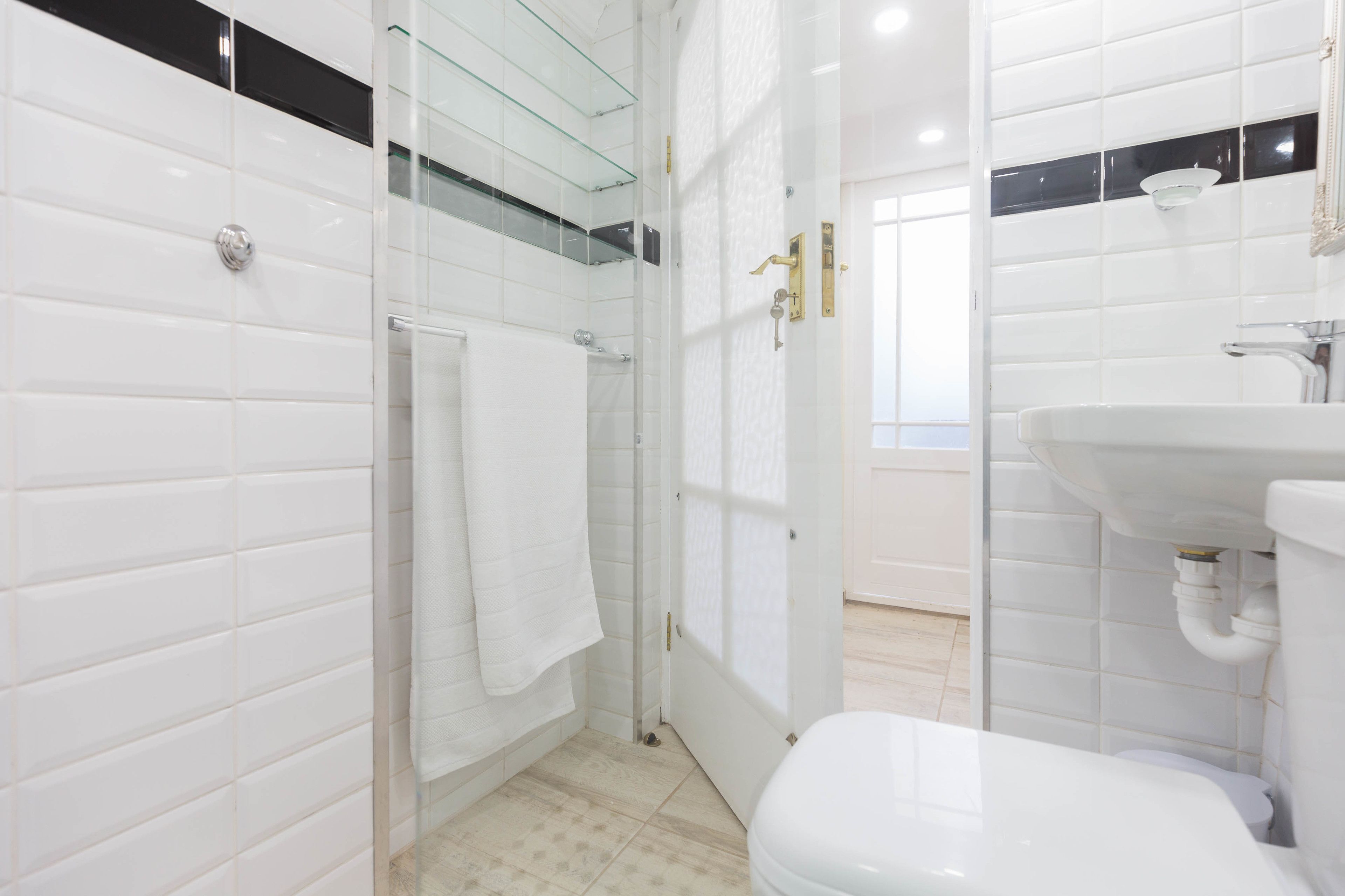 A modern bathroom with white tiles, a glass shower enclosure, a white toilet, and a sink with a mirror above it.