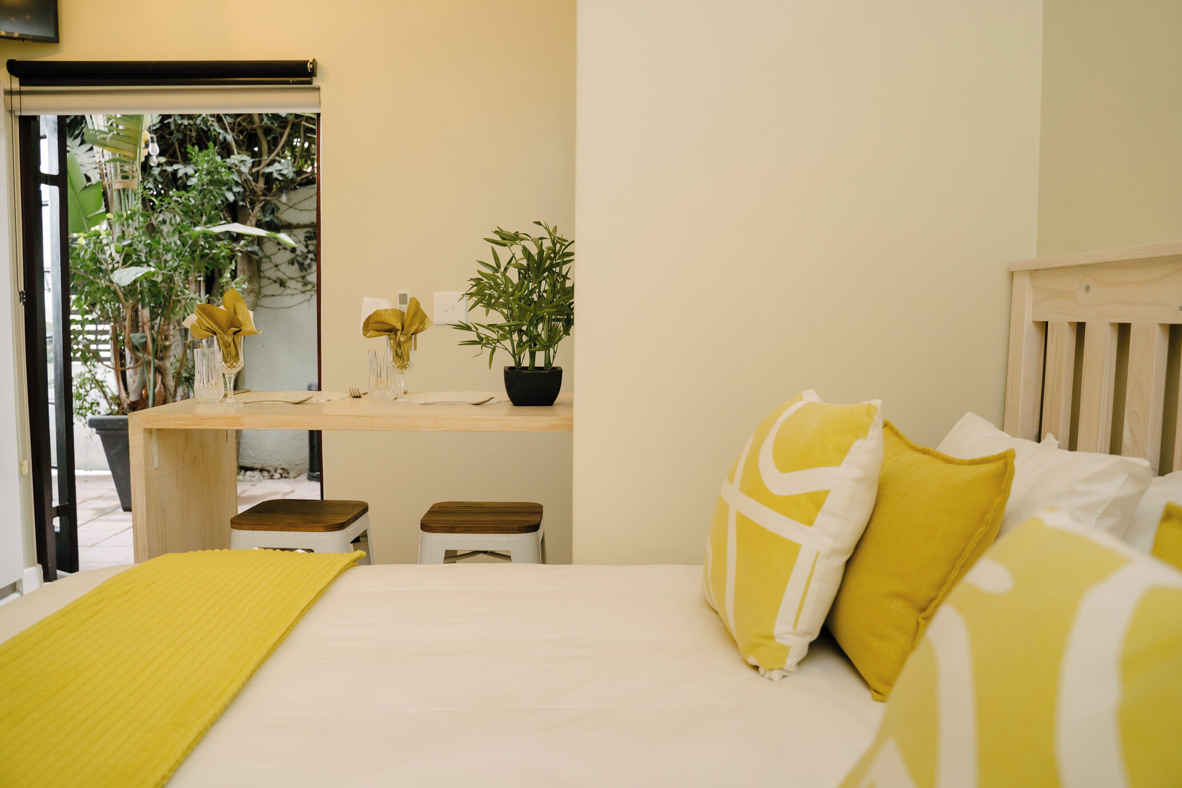 A bedroom with a bed, bedside table, and a window with a view of greenery.