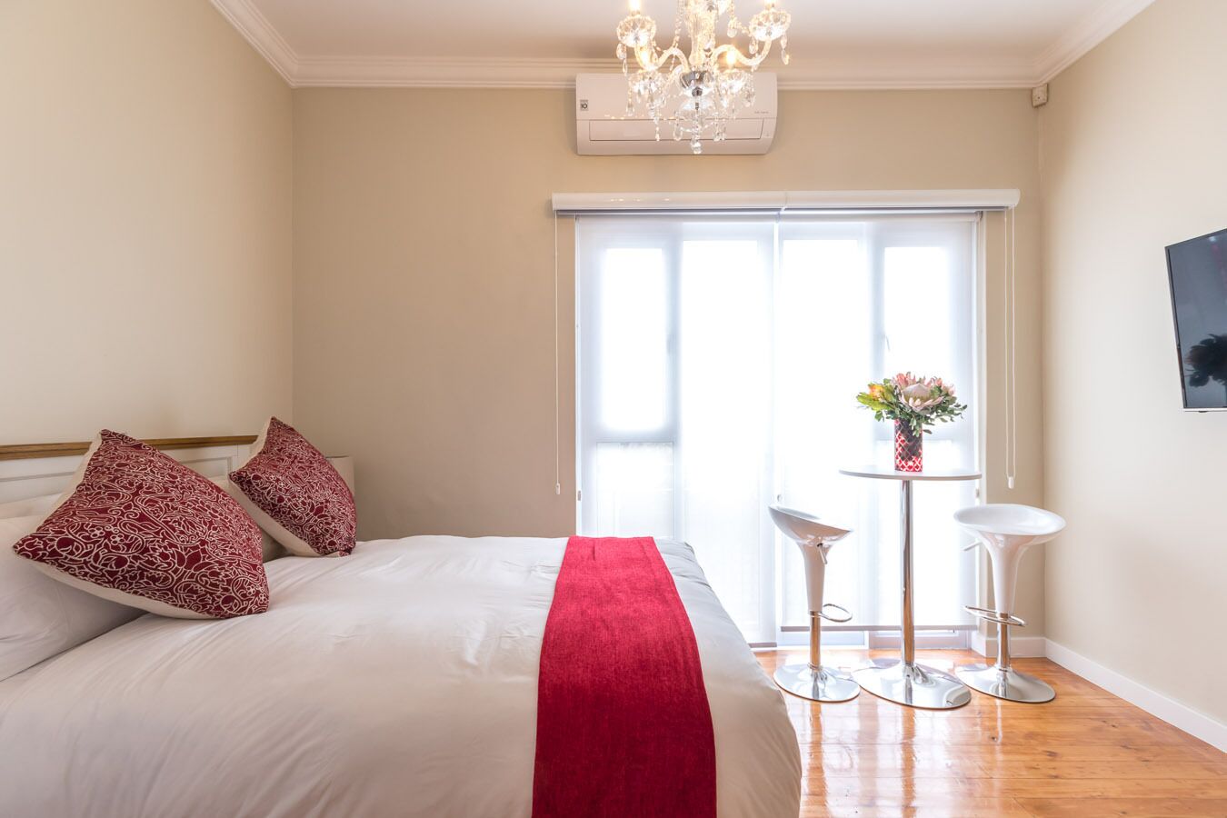 Ein Schlafzimmer mit einem Bett, einer roten Tagesdecke, zwei Nachttischen, einer Kristallleuchtre und einem Fenster mit Blick.