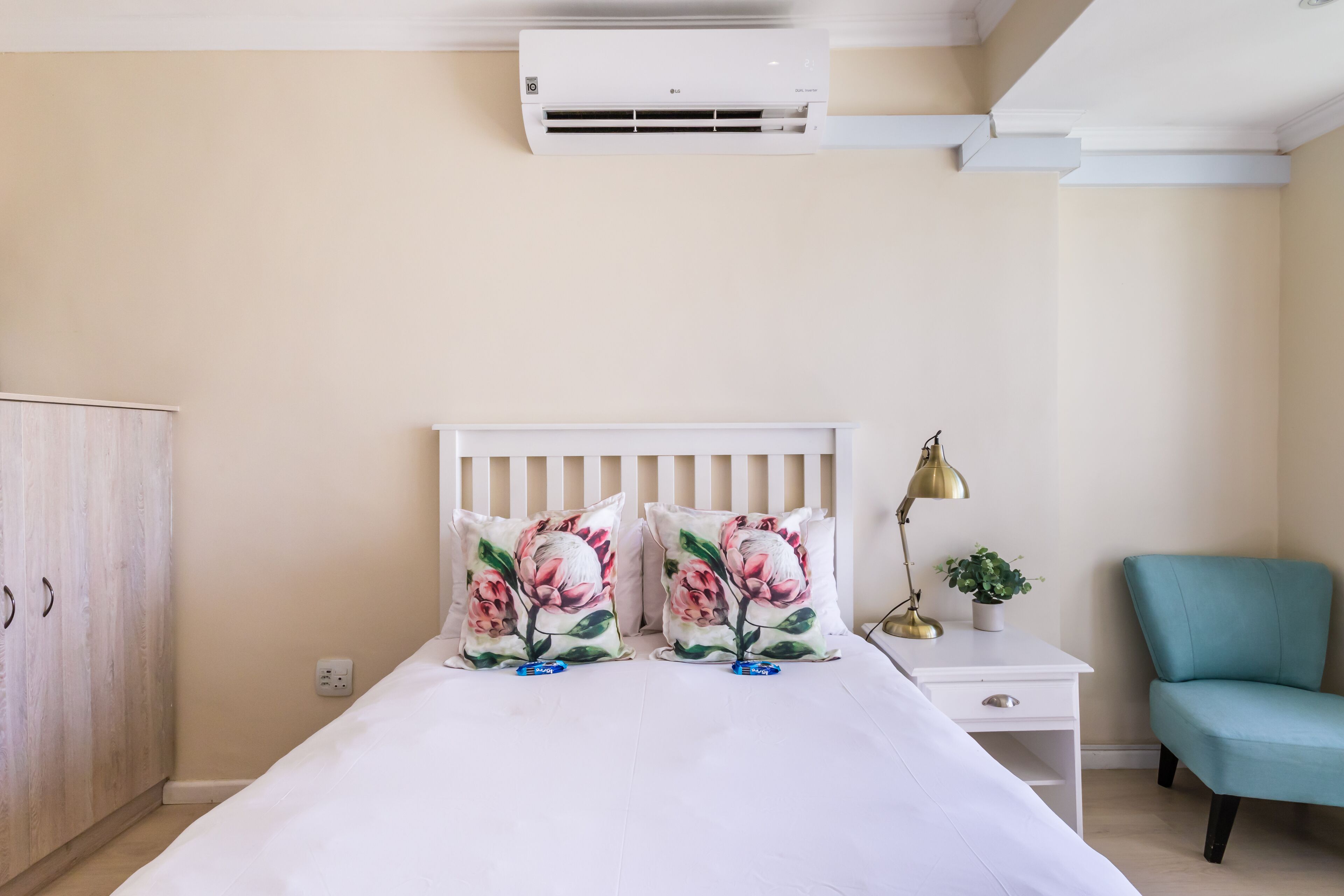 Un dormitorio con cama, mesita de noche, lámpara, silla y unidad de aire acondicionado.