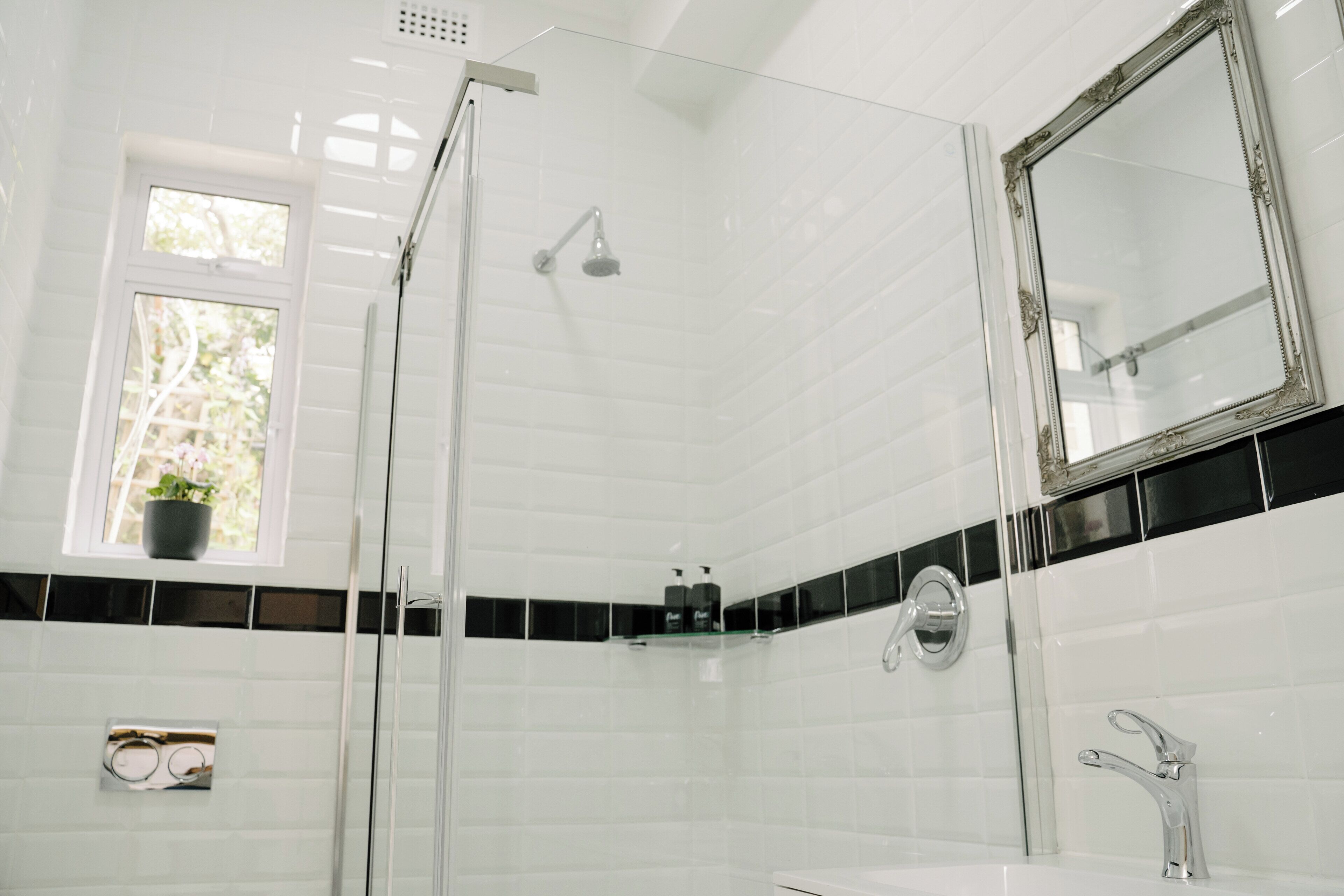 A modern bathroom with a glass shower enclosure, a white sink, and a large mirror.