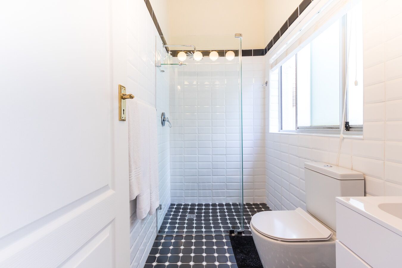 A bathroom with a glass shower enclosure, a white toilet, and a window providing natural light.