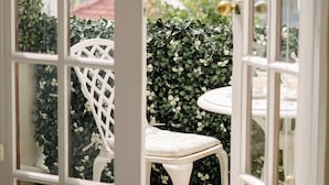 An open door leading to a patio area with a white chair and a table, surrounded by lush greenery. - Vesper Apartments (Cape Town)