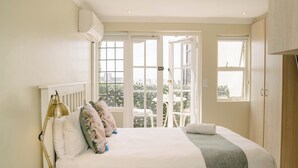A bedroom with a bed, bedside lamp, and a view of the outdoors through open doors. - Vesper Apartments (Cape Town)