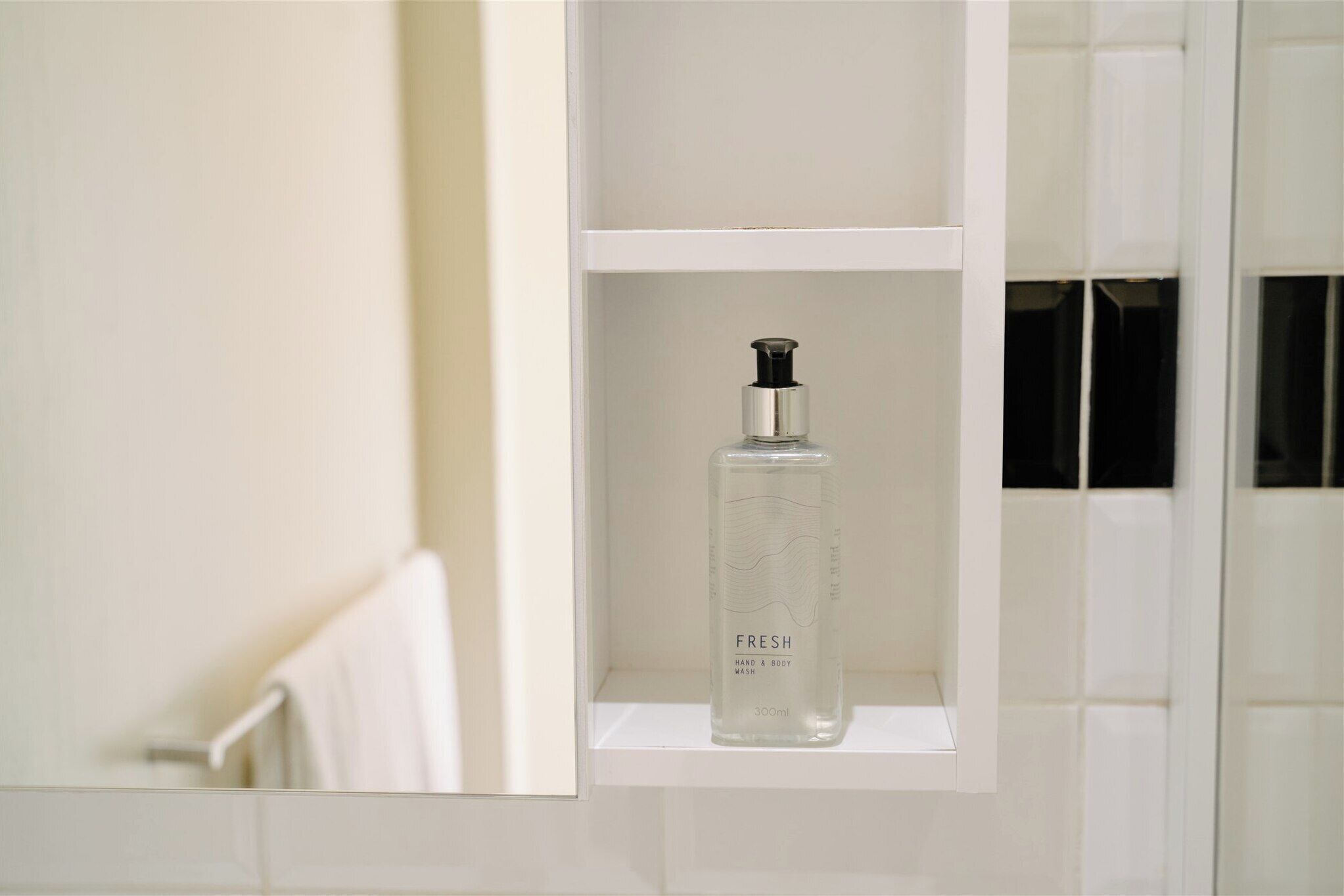 Ein Badezimmer mit einem weißen Regal, auf dem sich eine Flasche Hand- und Körperseife befindet.