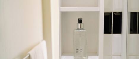 A bathroom with a white shelf containing a bottle of hand and body wash.