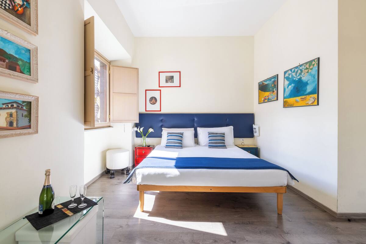 A bedroom with a bed, bedside tables, a glass cabinet, and artwork on the walls.