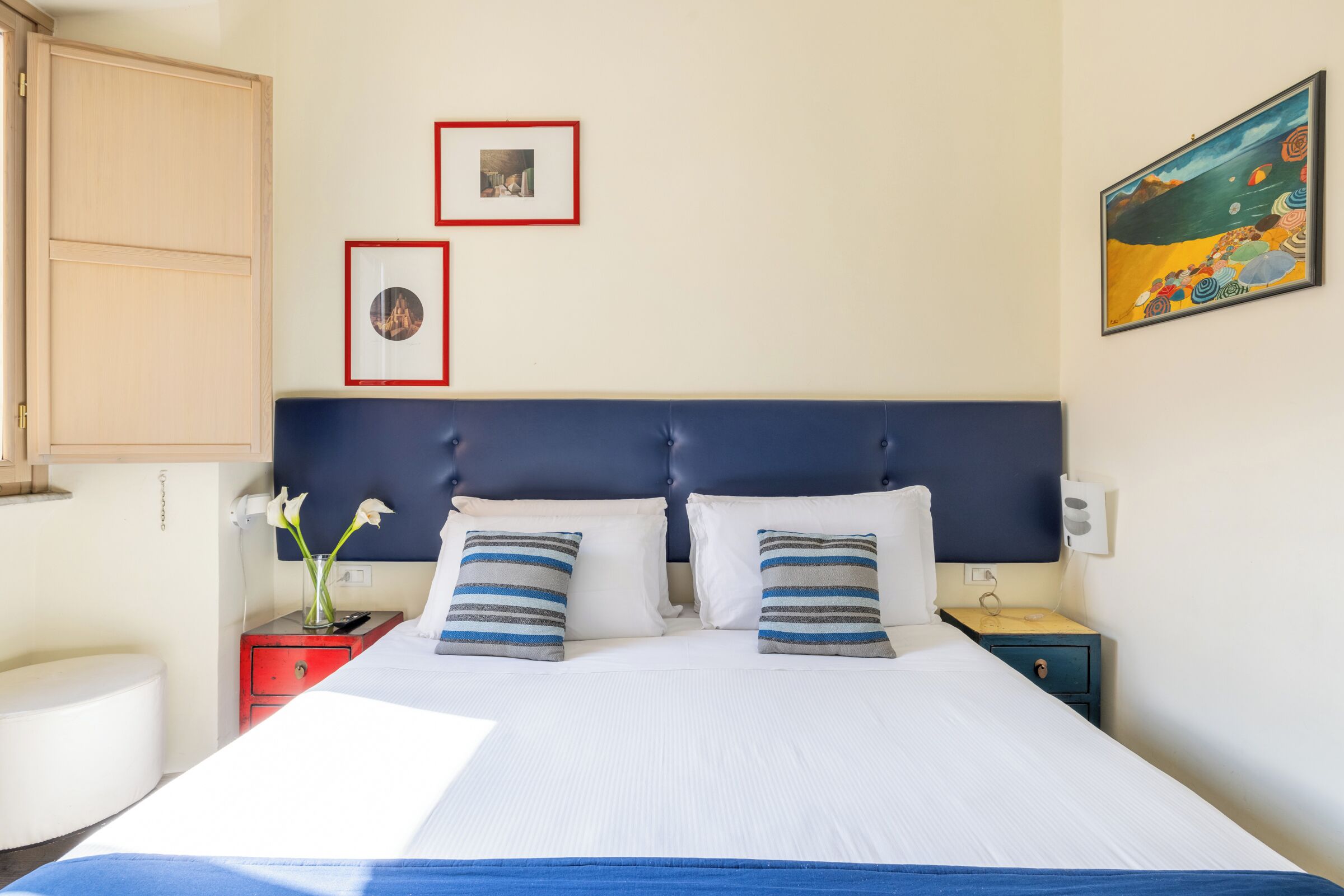 Ein Hotelzimmer mit einem Bett, zwei Nachttischen, einer roten Kommode und einer Wand mit zwei gerahmten Bildern und einem Gemälde.