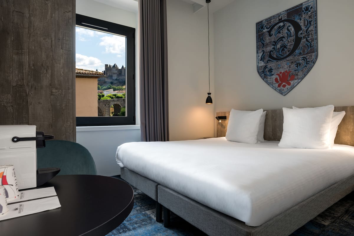 Ein Hotelzimmer mit Bett, Schreibtisch, Stuhl, einem Fenster mit Blick auf ein Schloss und einem dekorativen Schild an der Wand.