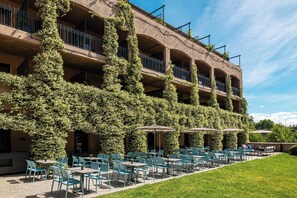 A building with multiple balconies covered in ivy, outdoor seating with umbrellas, and a well-maintained lawn. - SOWELL HÔTELS Les Chevaliers (Carcassonne)