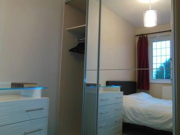 Un dormitorio con cama, armario y ventana con cortinas.