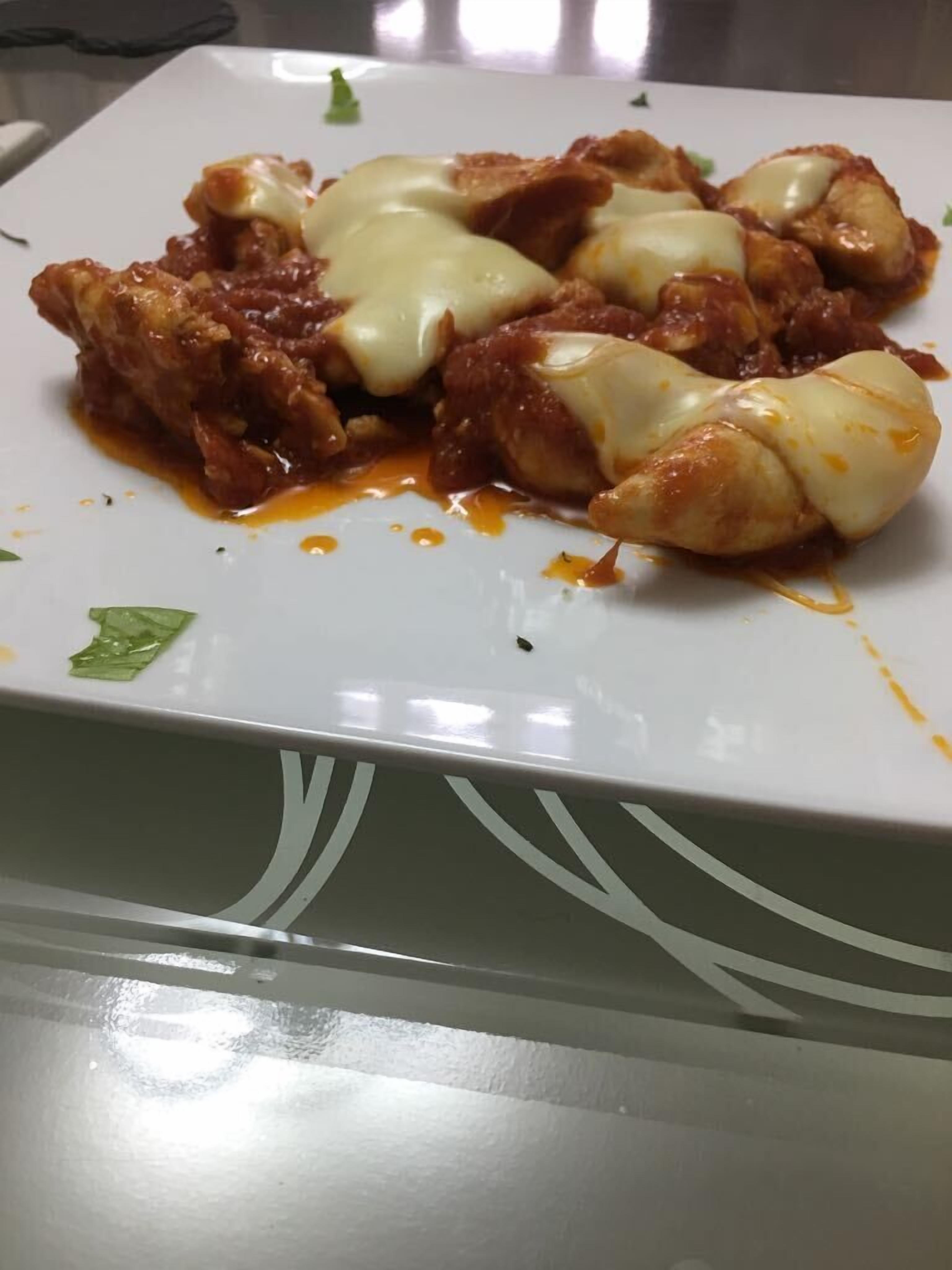 A white plate with a dish of chicken covered in sauce and cheese.