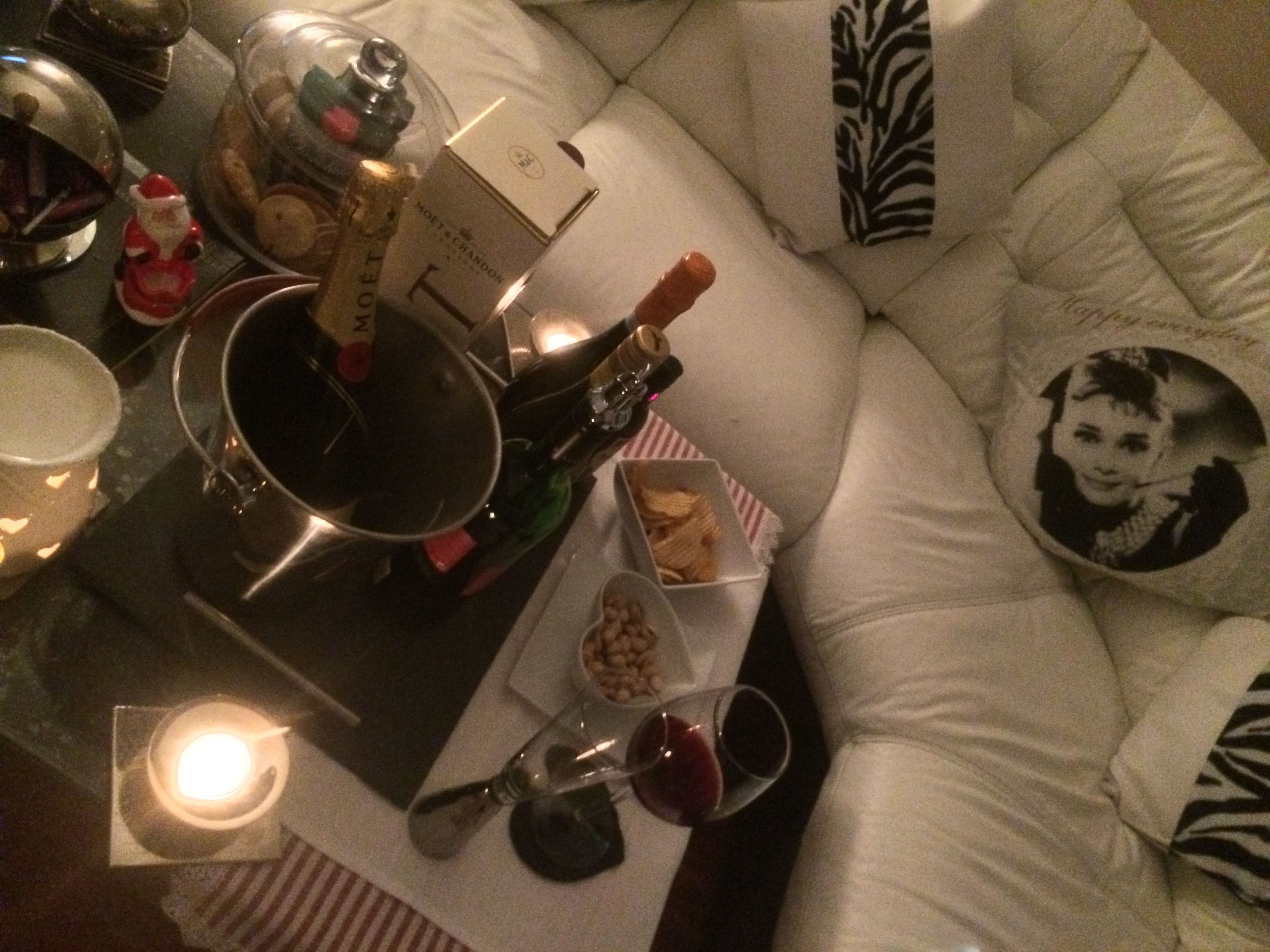 A cozy living area with a white sofa, a glass table with a bottle, a candle, and a tray with snacks.