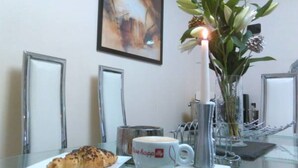 A glass table with a croissant, a cup of coffee, and a candle. - Bianca's House Hotel Heathrow Airport (Slough)