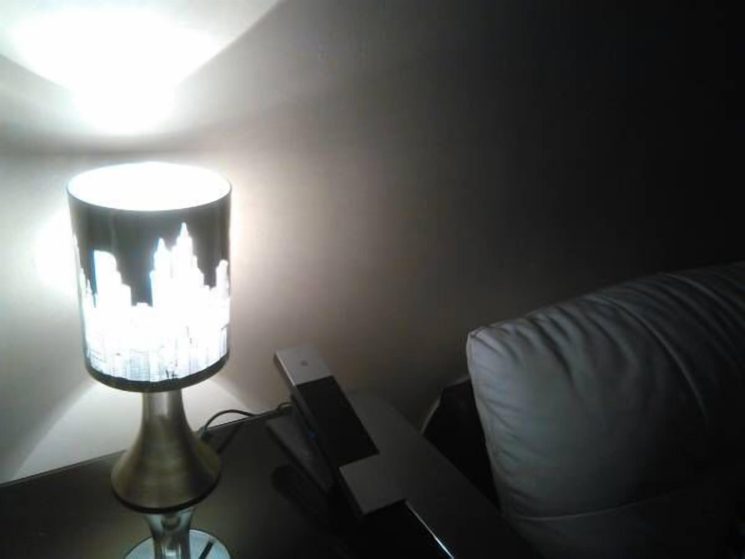 A lamp with a reflective surface on a bedside table next to a bed.