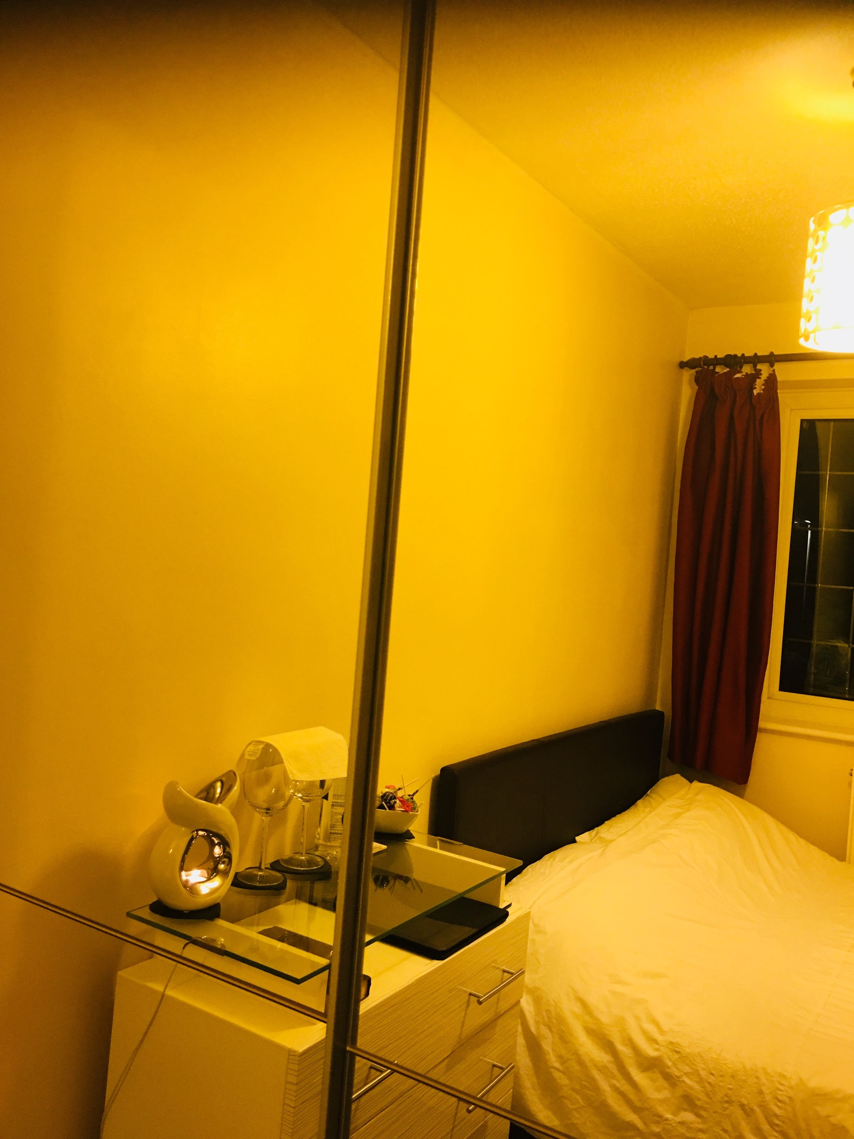 A hotel room with a bed, bedside table, and a window with curtains.