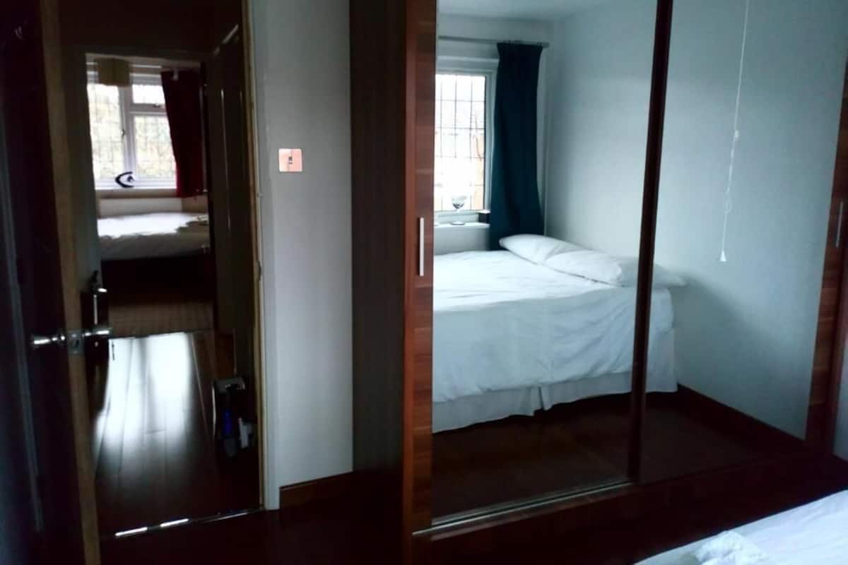 A room with a bed, a window with curtains, and a door leading to another room.