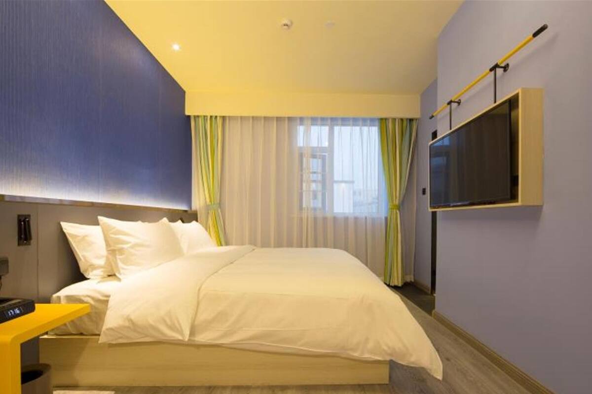 Ein modernes Hotelzimmer mit einem großen Bett, einem an der Wand montierten Fernseher und Holzboden.