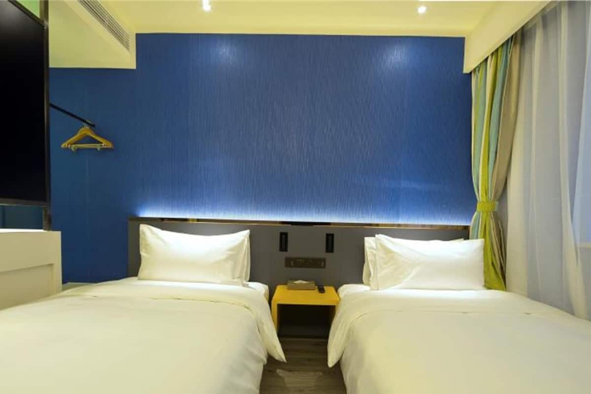 Ein Hotelzimmer mit zwei Betten, einem Nachttisch, einem Spiegel und einem Fenster mit Vorhängen.