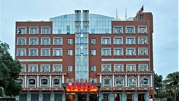 Un hôtel à plusieurs étages doté d’une façade centrale en verre, d’une conception symétrique des fenêtres et d’une entrée imposante avec une enseigne lumineuse.
