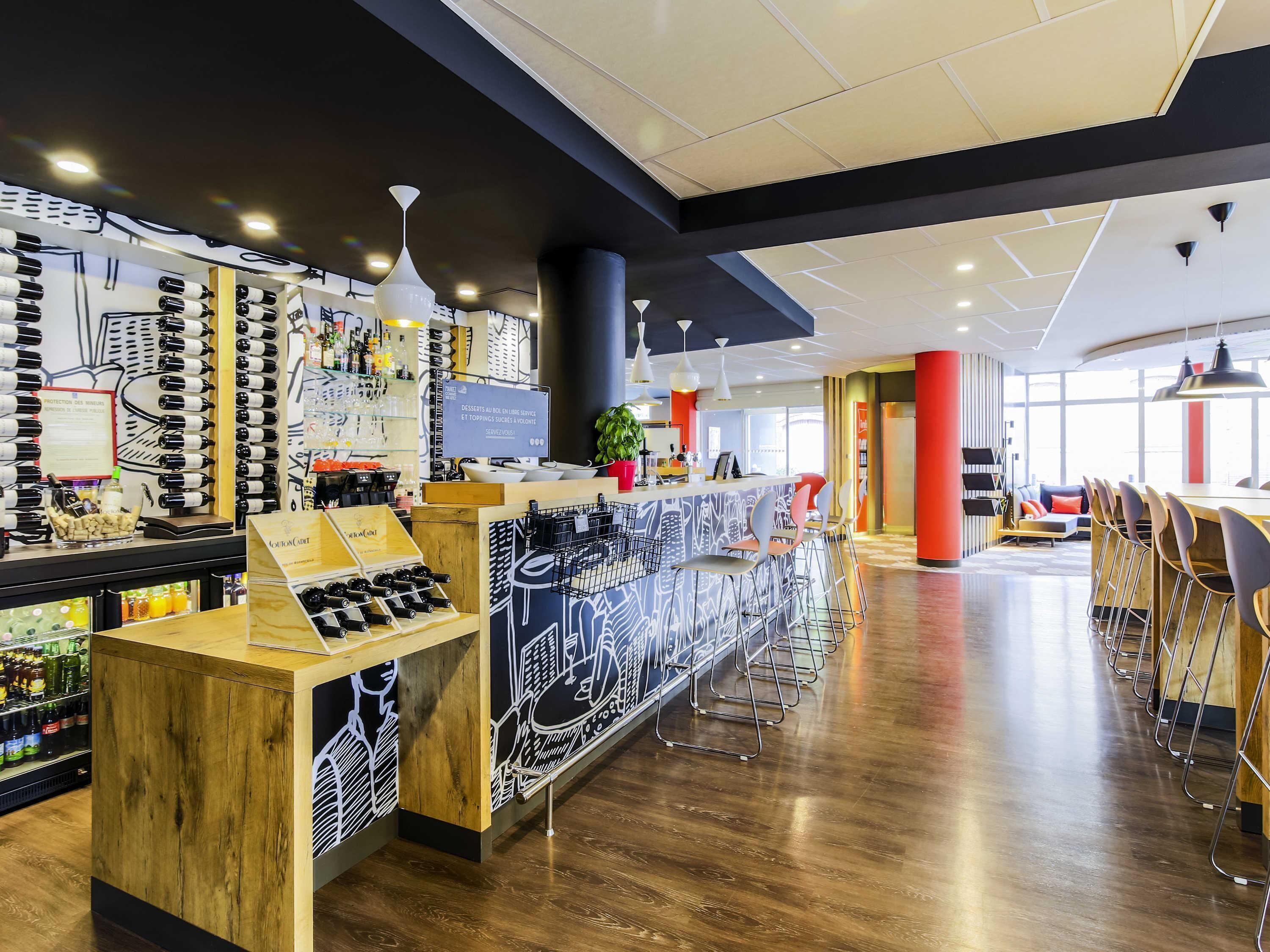 A modern bar area with a wooden counter, wine bottles, and a menu display.