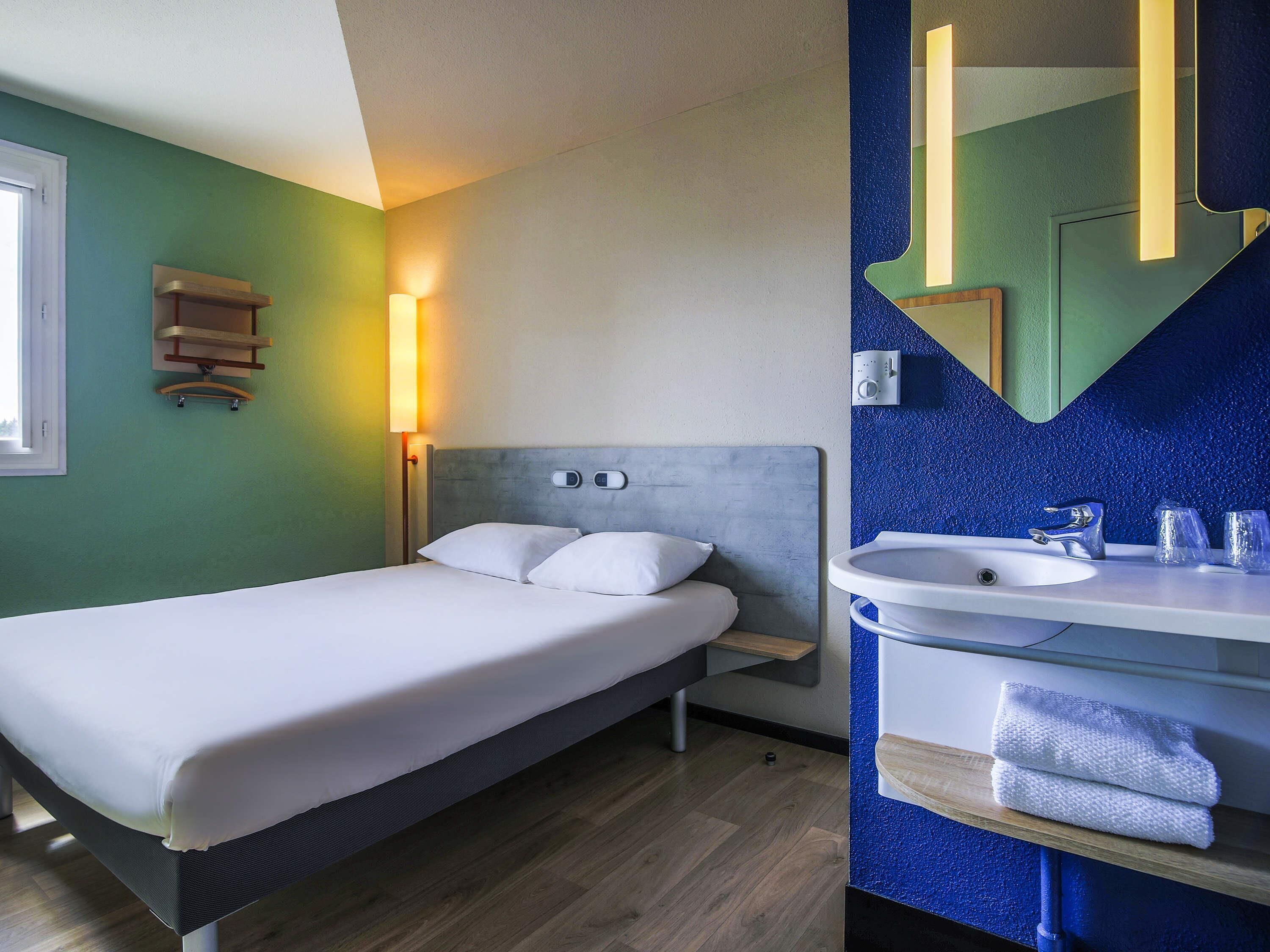A hotel room with a bed, bedside table, lamp, and a bathroom with a sink and mirror.