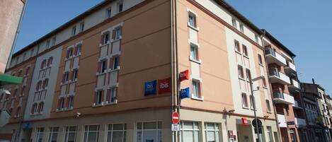 Un hotel de varios pisos con fachada color beige, múltiples balcones y varios letreros de 'Ibis'.