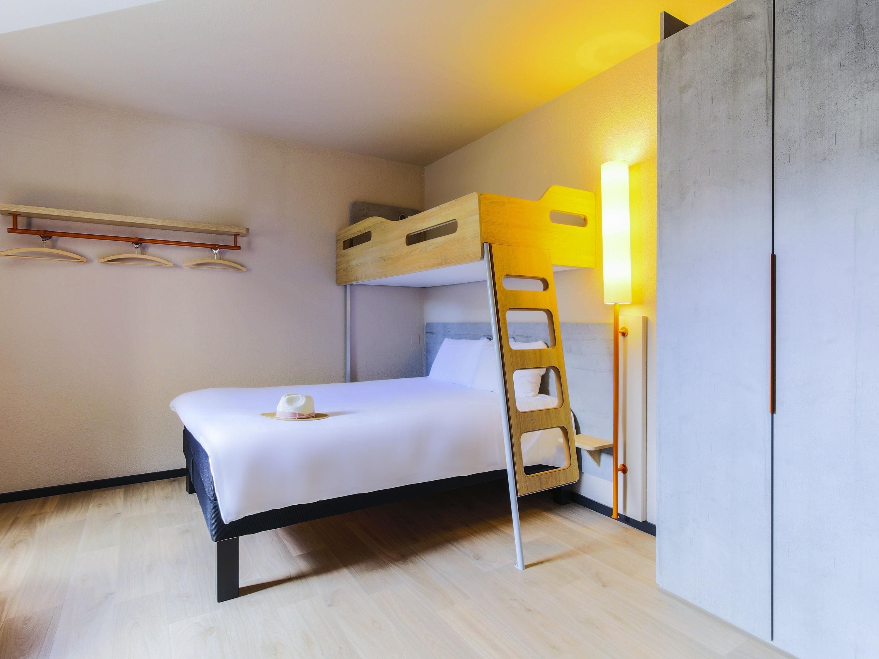 Un lit superposé avec une échelle, une table de chevet, une lampe et une armoire dans une chambre d’hôtel.