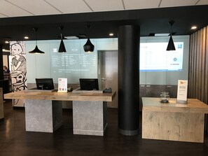 A modern hotel reception area with a large digital screen displaying information, a reception desk, and a large pillar. - ibis budget Albi Centre (Albi)