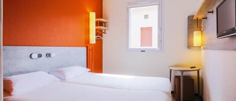 A hotel room with a bed, bedside controls, a small table, a TV, and a window.