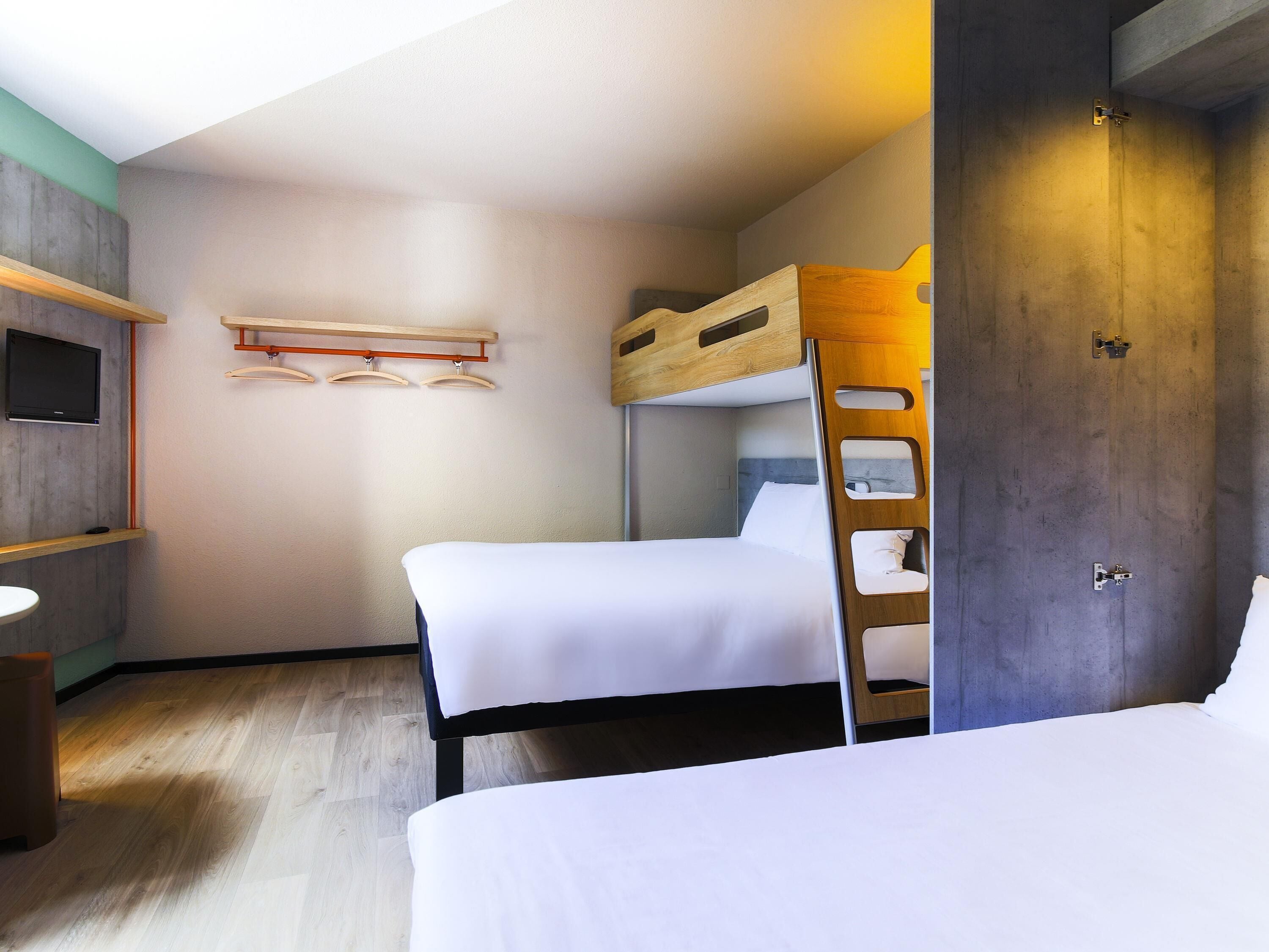 Ett hotellrum med två sängar, en våningssäng i trä, en tv som är monterad på väggen och en dörr i trä.