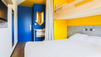 Habitación de hotel con literas, un baño con espejo y lavamanos, y una puerta que da a otra habitación.