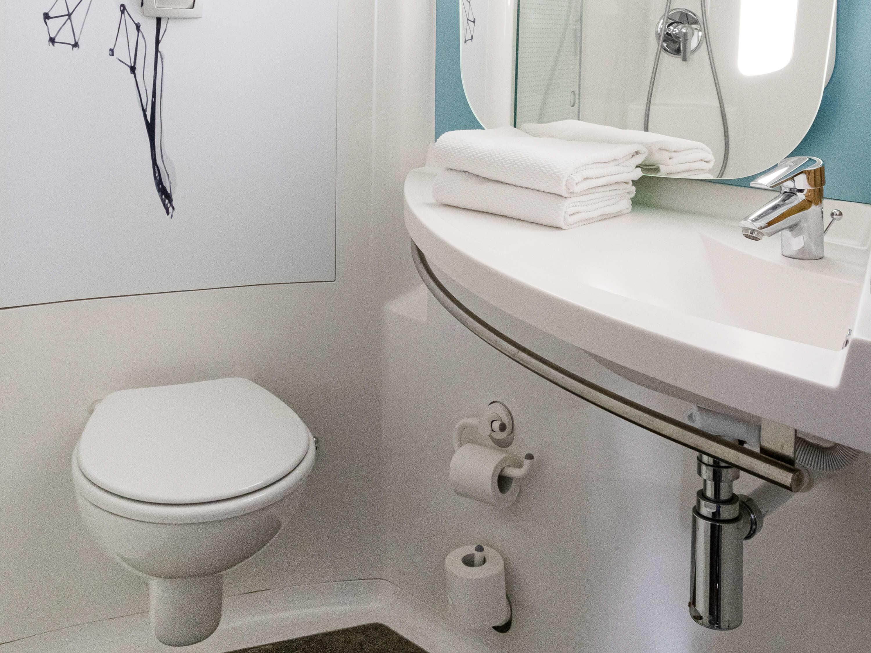 Un baño con un inodoro blanco, un lavabo con espejo y dos rollos de papel higiénico.