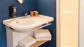Un baño con lavamanos blanco, un espejo, toallero y una botella de champú.