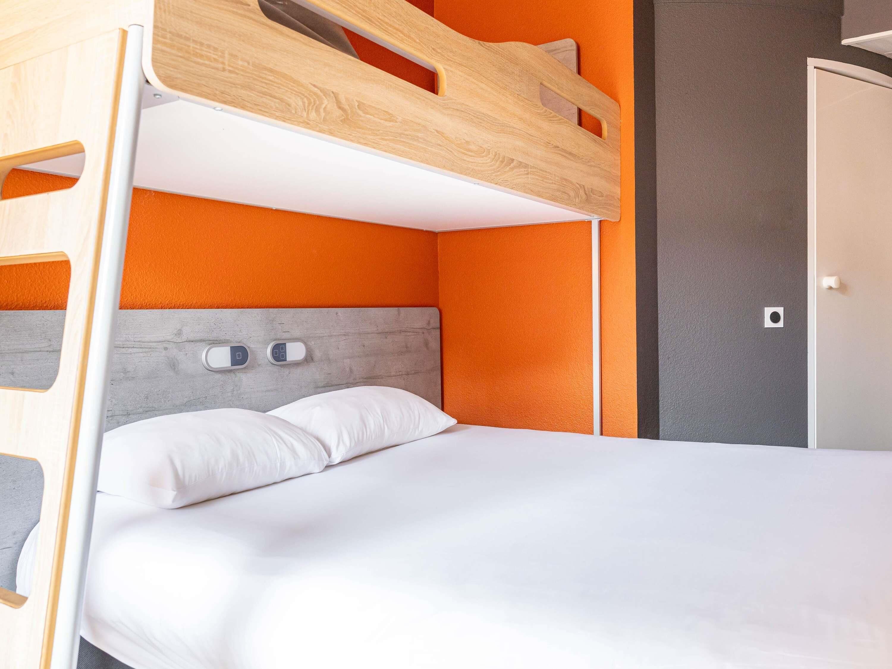 A bunk bed with a wooden headboard, white bedding, and an orange accent wall.