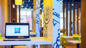 Una computadora portátil sobre una mesa que muestra el logotipo de ibis budget hotels, con un interior moderno que incluye arte abstracto en las paredes y zonas de estar.