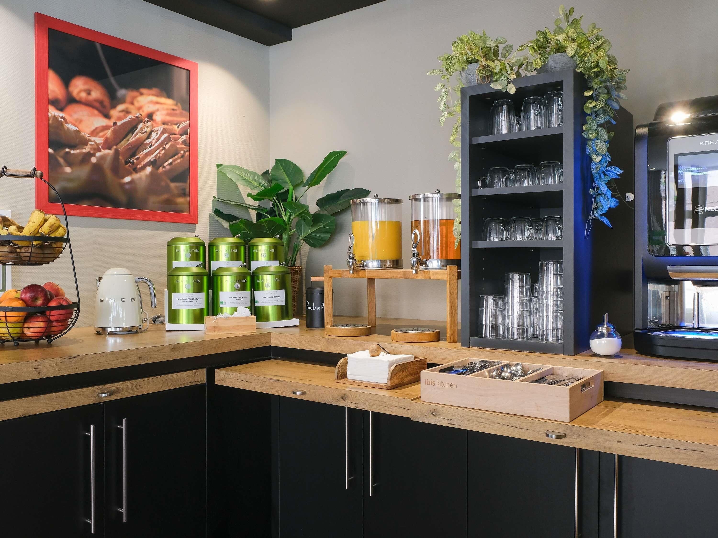 A kitchen with a coffee machine, fruit basket, green canisters, a juice dispenser, and a coffee machine.