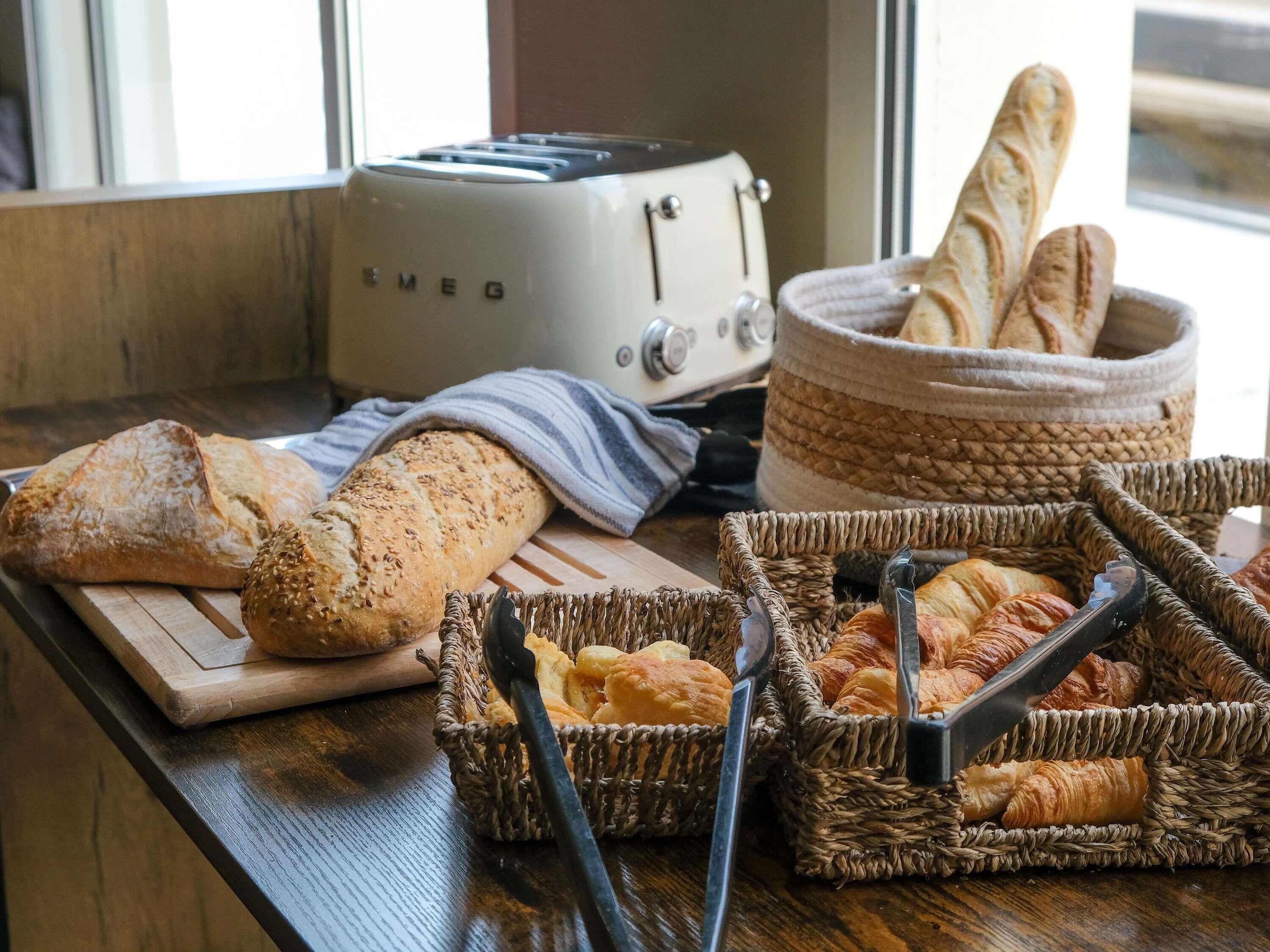 Un plan de travail de cuisine avec une miche de pain, un grille-pain et des paniers remplis de viennoiseries.