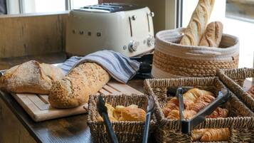 Un plan de travail de cuisine avec une miche de pain, un grille-pain et des paniers remplis de viennoiseries.