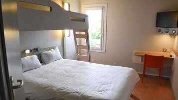 Habitación de hotel con literas, un escritorio con silla, televisor montado en la pared y ventana que deja entrar luz natural.
