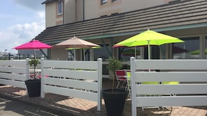Un espace patio agrémenté de clôtures blanches, de plantes en pot et de parasols colorés.
